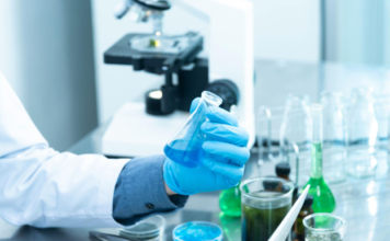 Revolutionizing Agriculture: The Rise of Agri-Tech Lab Spaces A scientist wearing blue gloves holding a glass flask with blue liquid in a research laboratory, surrounded by test tubes and beakers with various colored solutions.