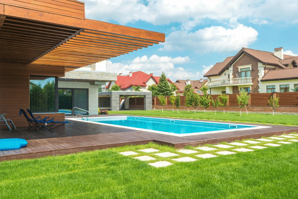 Luxury backyard with in-ground swimming pool, contemporary wood deck, manicured lawn and stone walkway in a suburban neighbourhood.